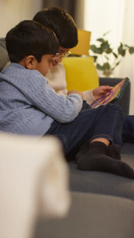 Vertical-Video-Of-Two-Young-Boys-Sitting-On-Sofa-At-Home-Playing-Games-Or-Streaming-Onto-Digital-Tablet-Together-3